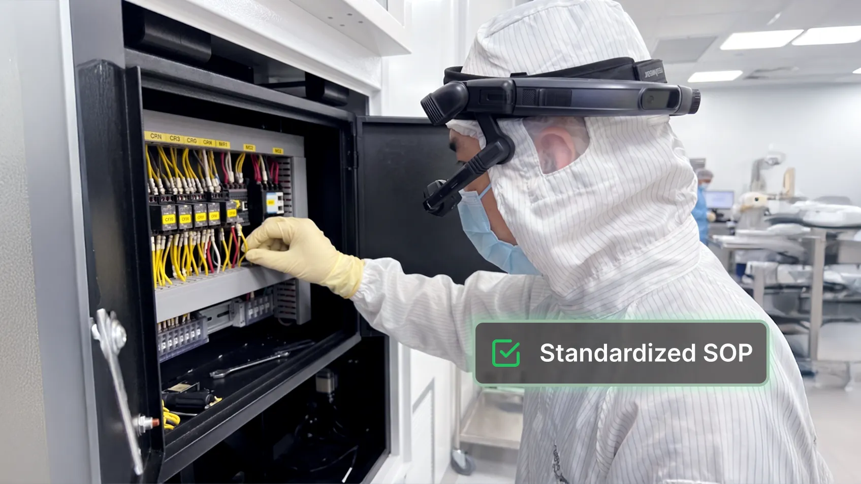 A cleanroom technician wearing smart glasses and gloves works on electrical panel wiring.